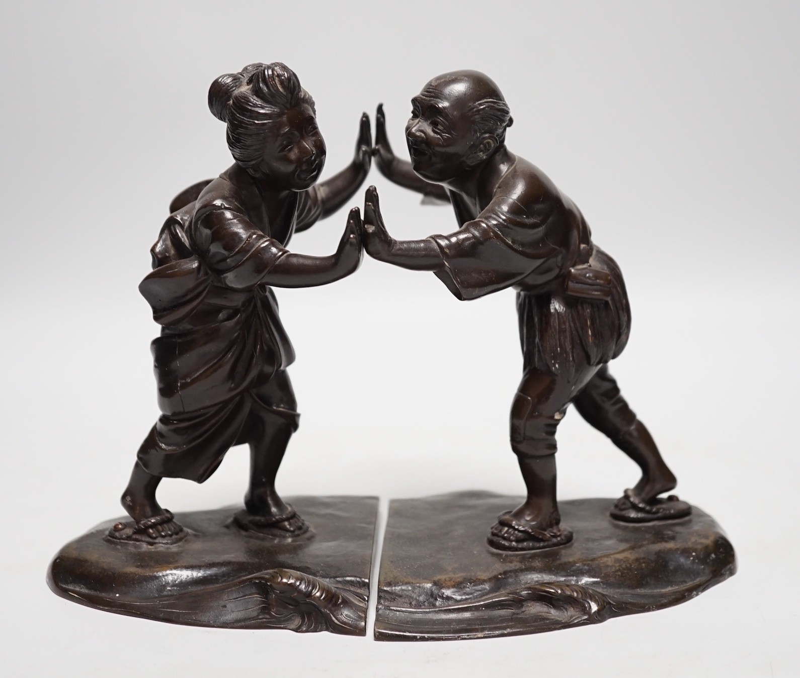 A pair of Japanese Meiji period bronze bookends modelled as a husband and wife pushing against each other, 18cm